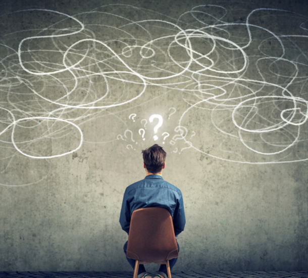 Man in a chair looking a a wall with question marks.