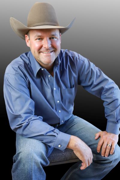 Sach Oliver leaning forward wearing a cowboy hat, a blue shirt and jeans