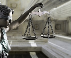 Metal scales of justice held by a statute with marble columns in background.